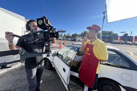 A camera operator with a stabilized rig filming an actor by a car