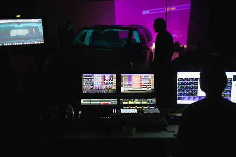 Monitors and a lighting desk in front of a car on a dark stage